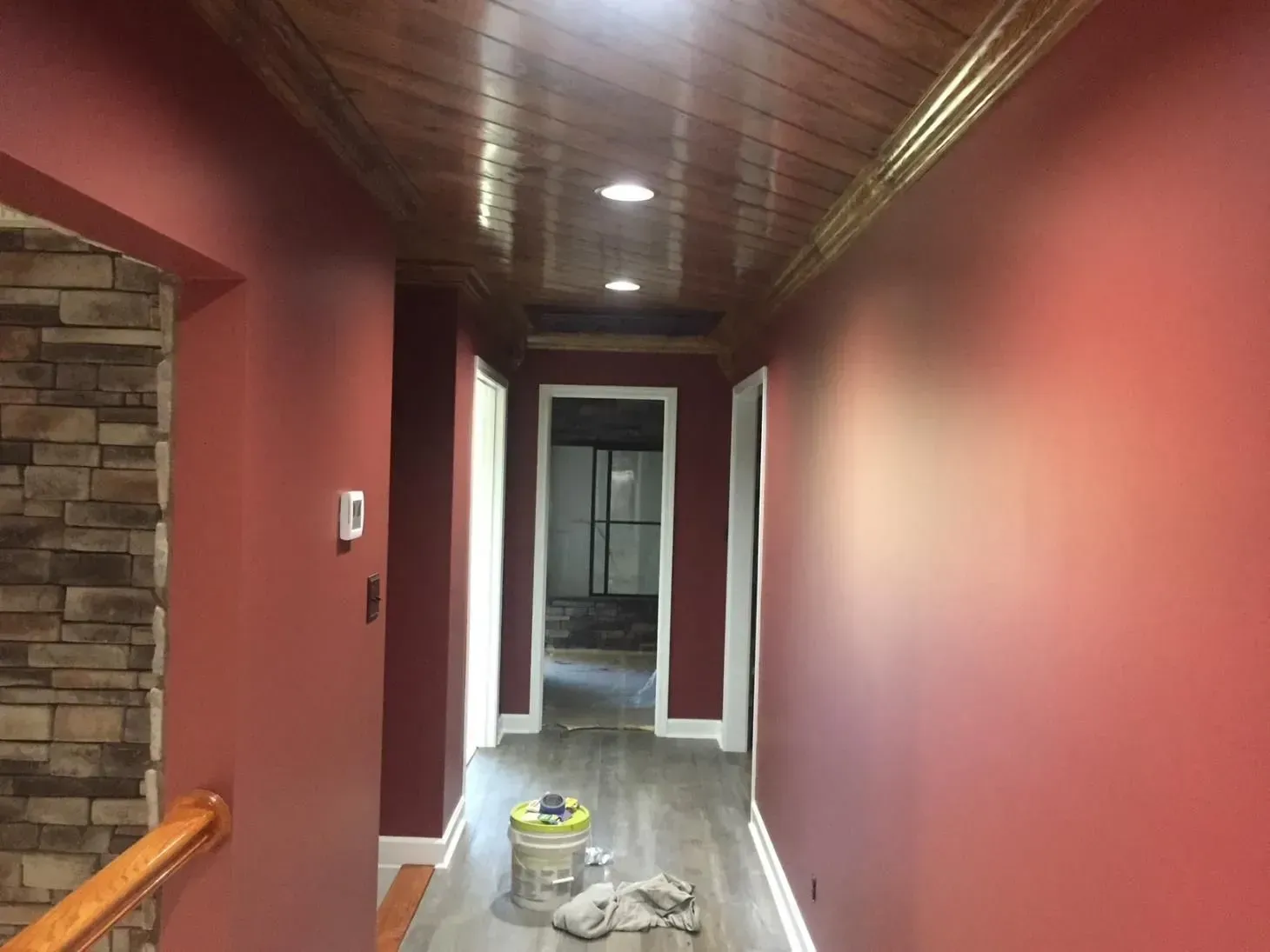 Long hallway with red walls, a wood ceiling, and a light-colored floor. A stone wall is visible on the left.