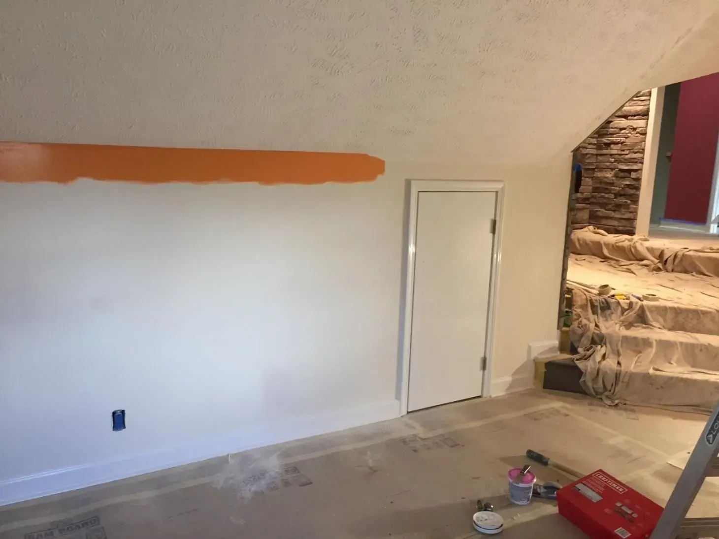 Interior view of a room with a white wall, a painted orange stripe, a white door, and stone steps.