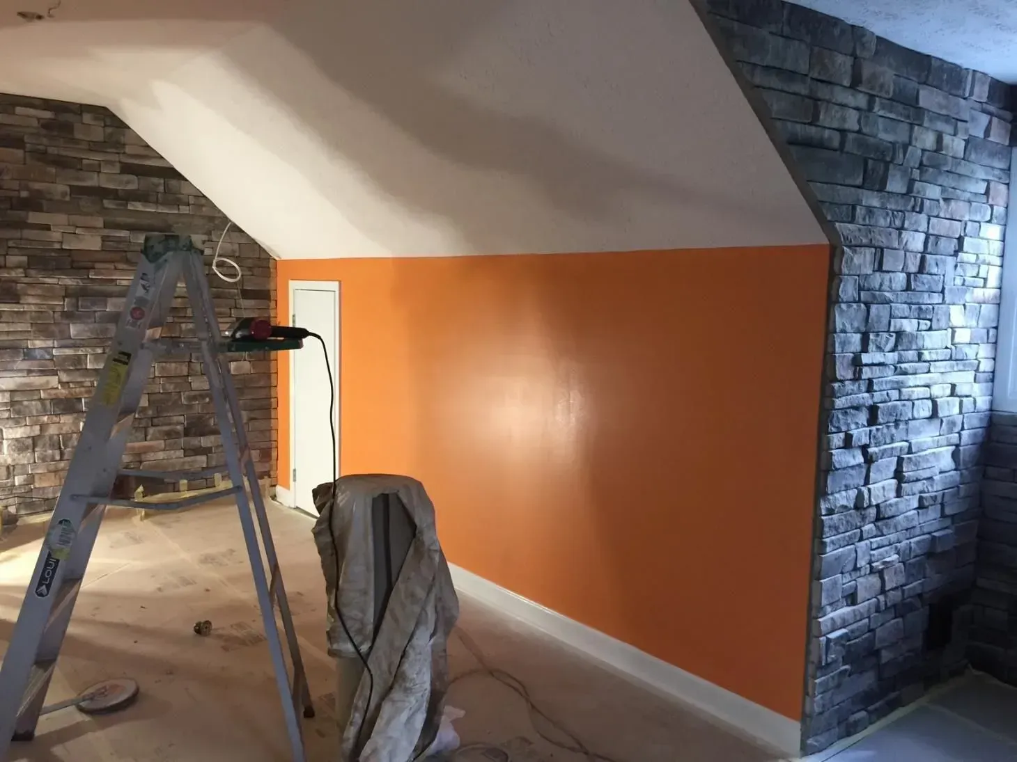 Interior of a room with an orange wall, stone accent walls, and a ladder. The ceiling is white.