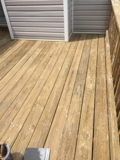 Wooden deck with peeling paint next to a structure with light grey siding. Paint bucket and brush are visible.