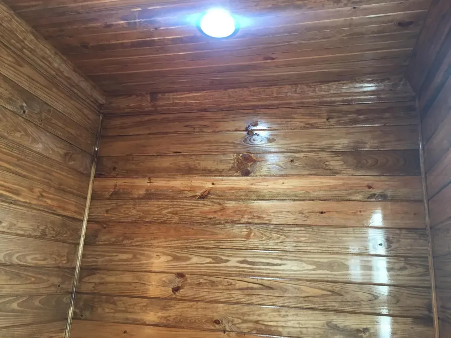 Wooden interior with a bright light fixture. Horizontal wood planks cover the walls and ceiling, reflecting light.
