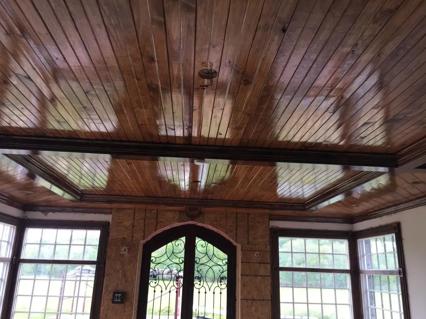 Wooden ceiling with glossy finish, light reflecting from it. Arched doorway and windows with a view of greenery.