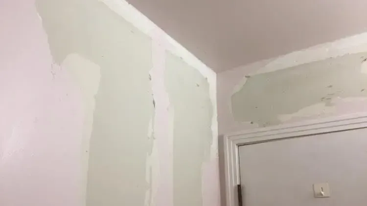 A corner of a room with pink walls where drywall has been repaired, showing patches of light green compound.