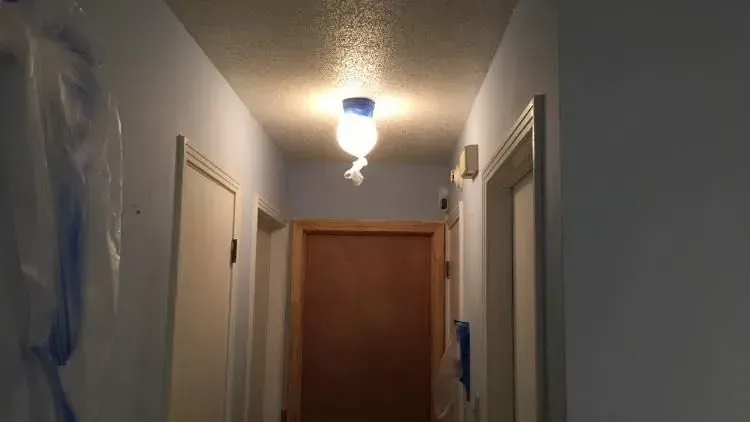 A narrow hallway with a single light fixture. The walls are light blue, with three closed doors.