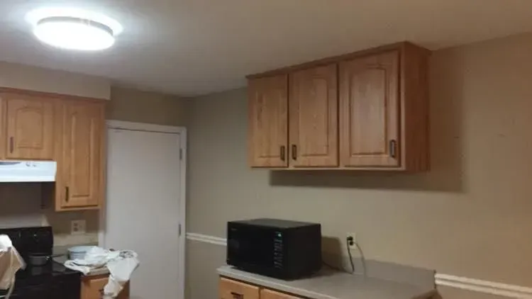 A kitchen interior with light-colored cabinets, a microwave, and a white door. Beige walls and a light fixture are also visible.