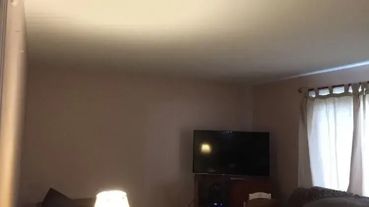 A living room with a TV on the wall, curtains, and a lamp, with soft lighting and a neutral color scheme.