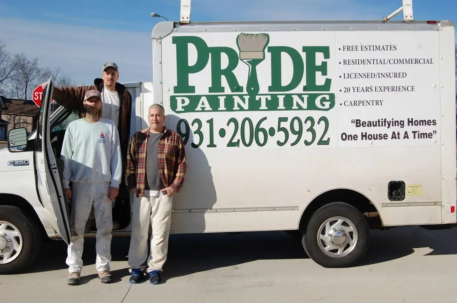Three painters stand with a Pride Painting truck. The truck is white with green lettering and a phone number.