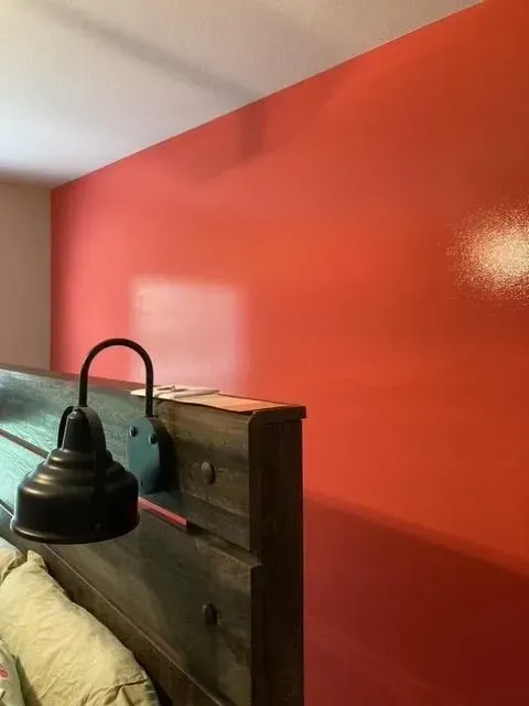 A bright orange wall with a black sconce attached to a wooden headboard.