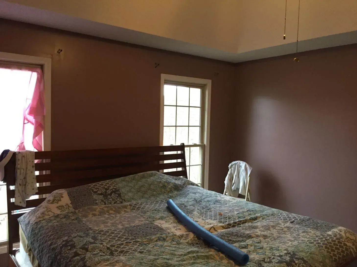 Bedroom with brown walls, a bed with a patchwork quilt, and two windows with curtains.