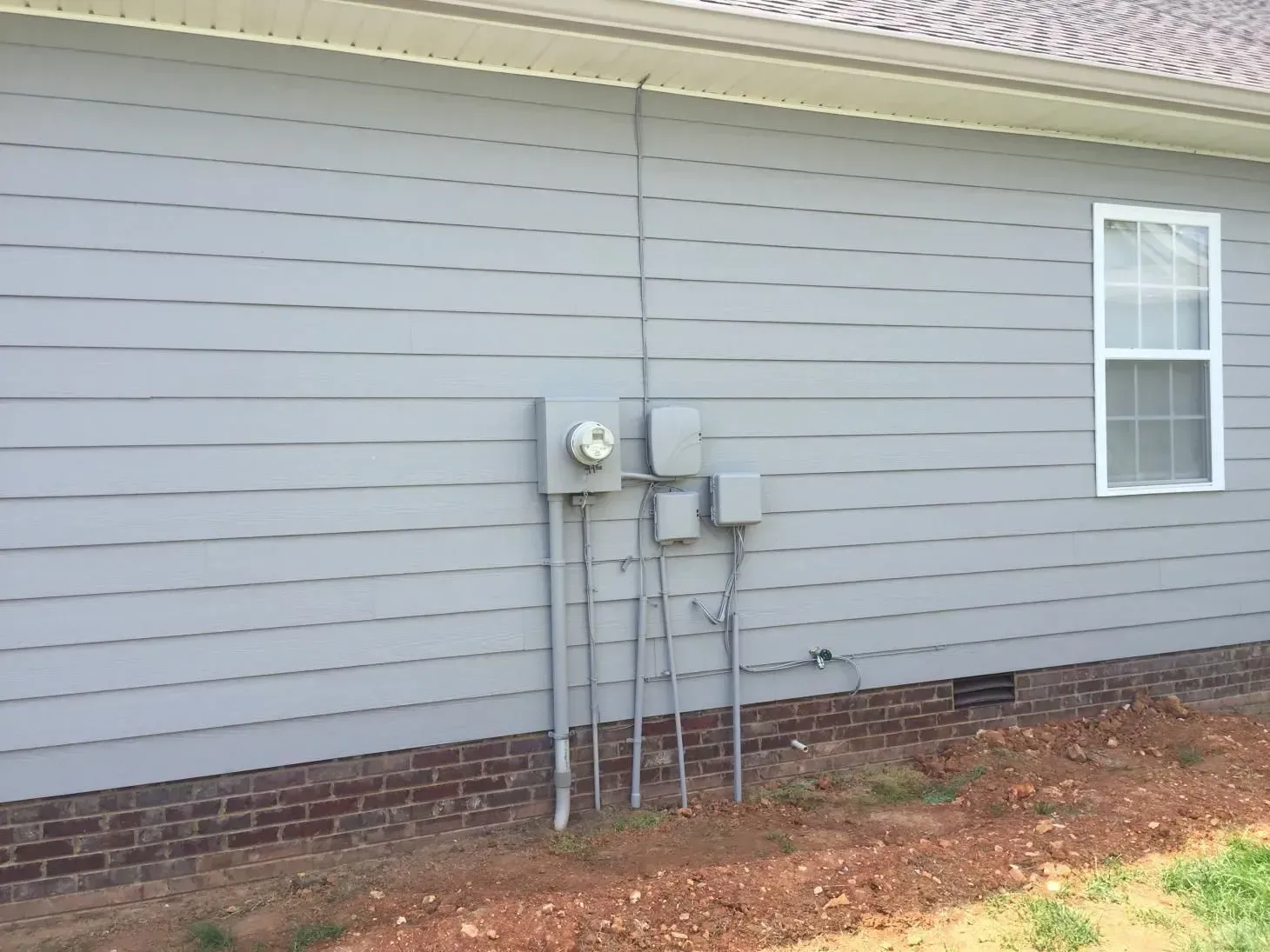Gray siding with electrical boxes and a window on a residential building. Conduit runs up the side of the house.