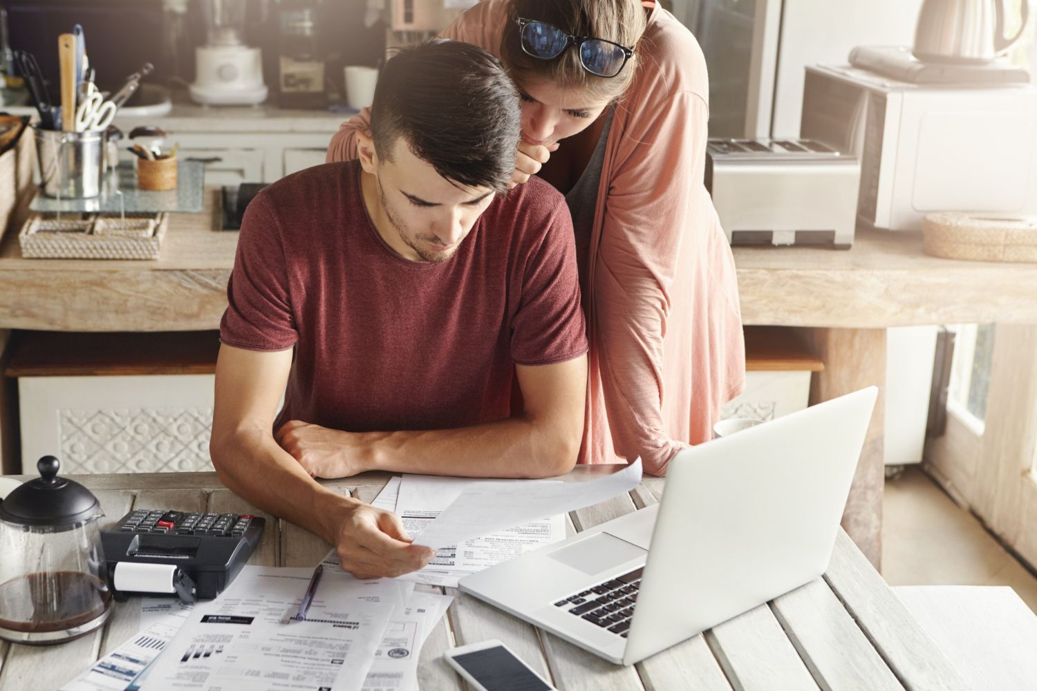 Couple reviewing finances together at a table with laptop, receipts, and calculator.