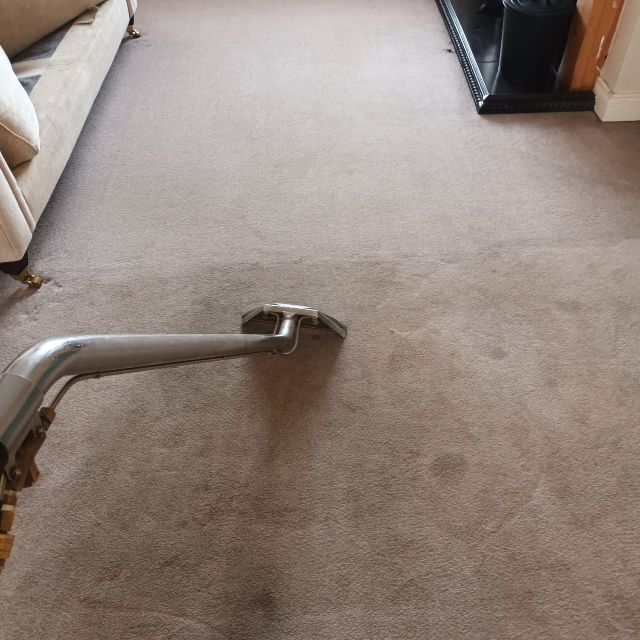 A vacuum cleaner is cleaning a carpet in a living room