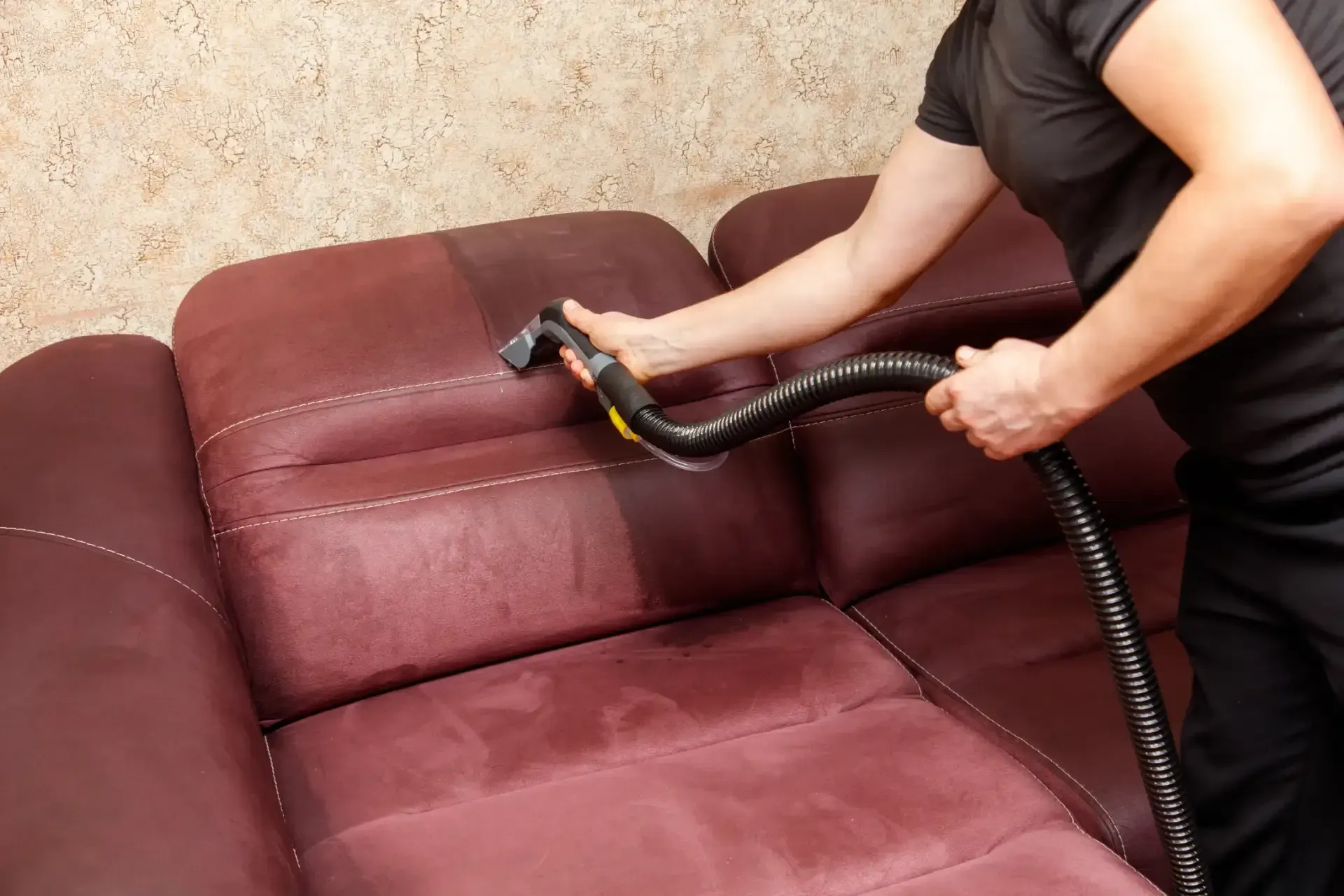 A woman is cleaning a couch with a vacuum cleaner.