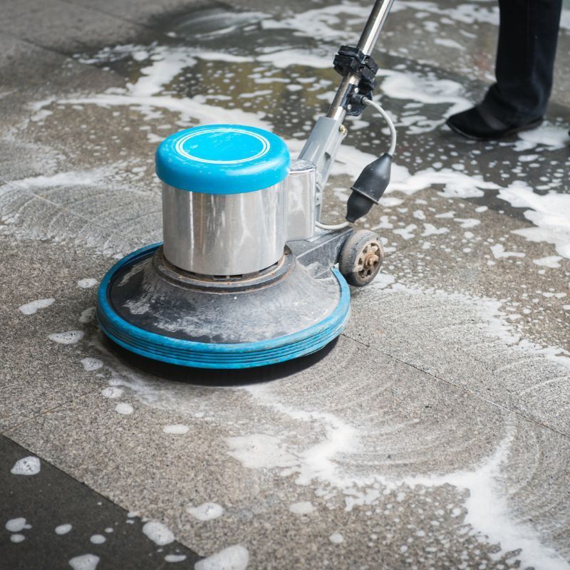 A person is cleaning a concrete floor with a machine.