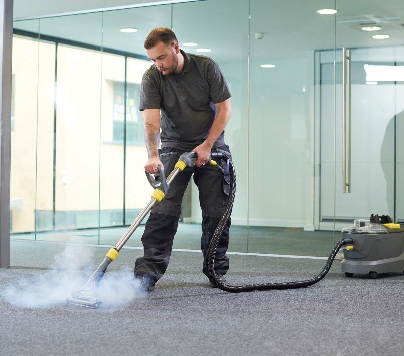 A man is cleaning a carpet with a vacuum cleaner.