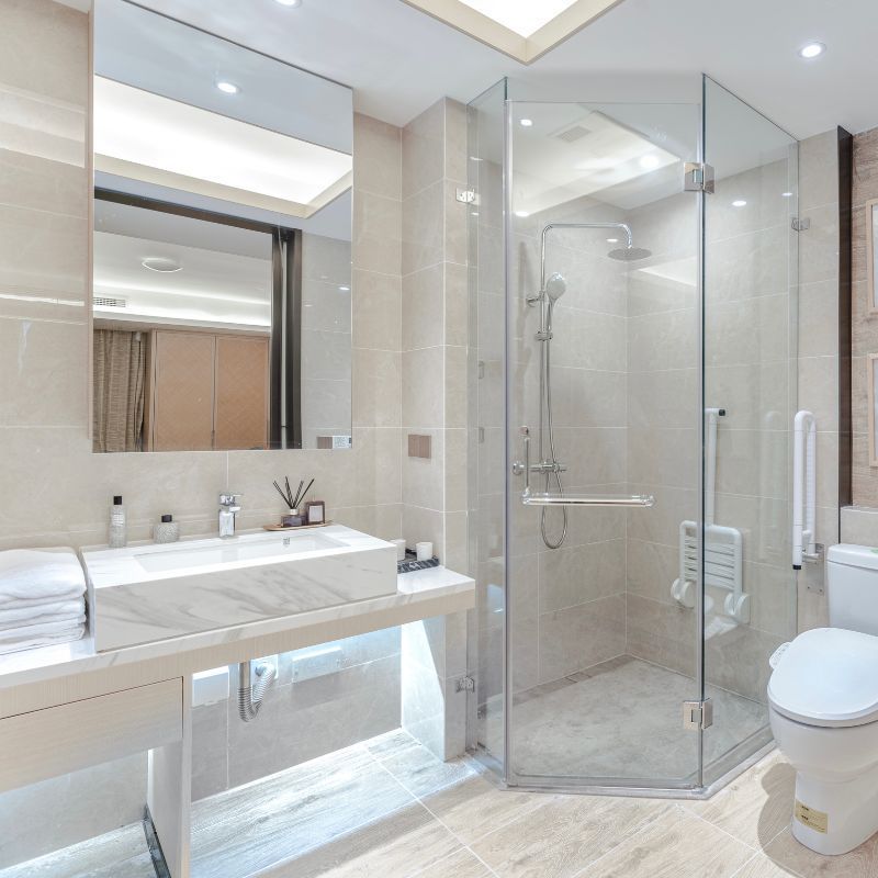 Modern bathroom with marble vanity, glass shower, and toilet. Neutral tones, bright lighting.