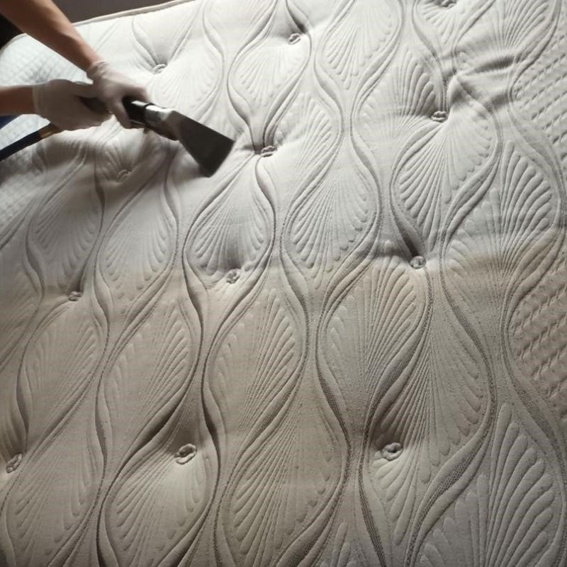 A person is cleaning a mattress with a vacuum cleaner.