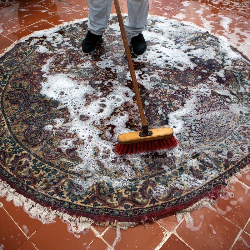 A person is cleaning a rug with a broom