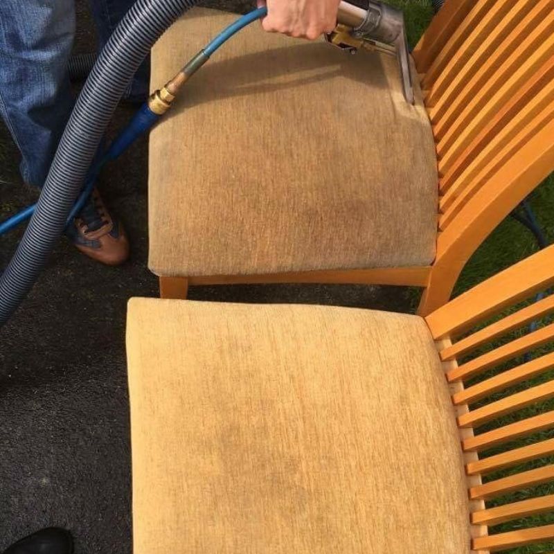 A person is cleaning a chair with a vacuum cleaner.