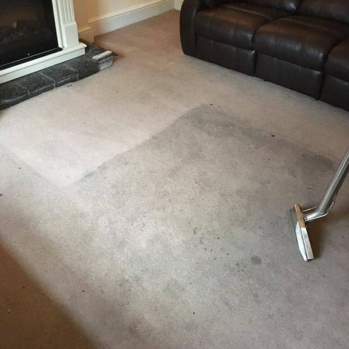 A vacuum cleaner is being used to clean a carpet in a living room.