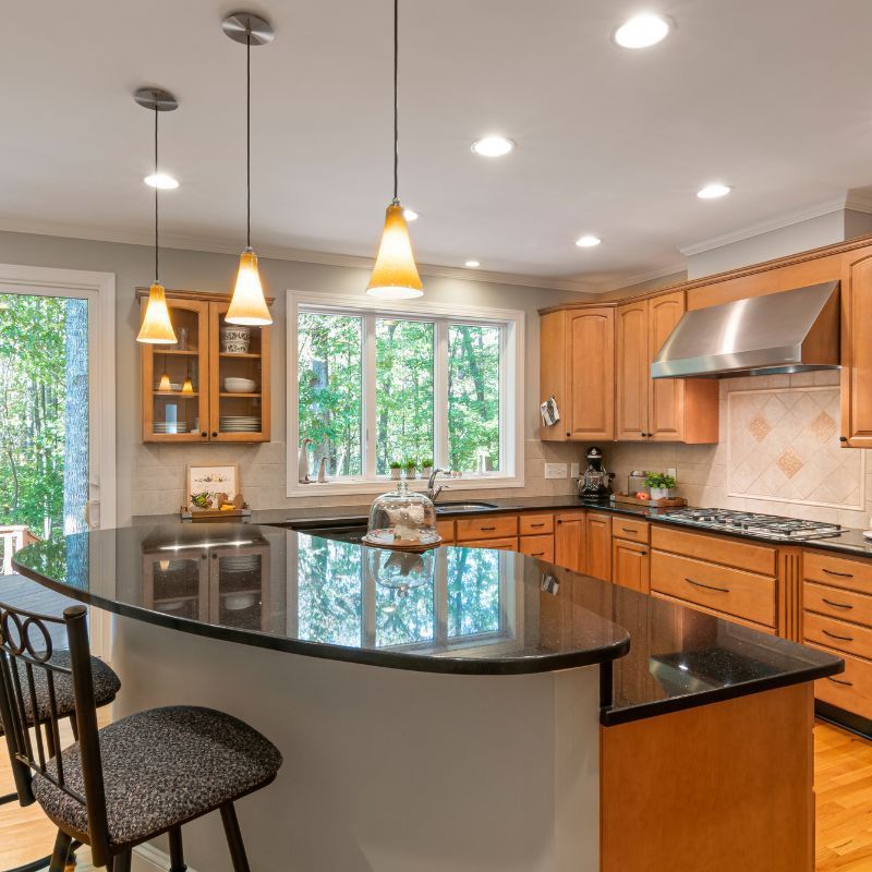Kitchen with a black countertop island, wooden cabinets, and three pendant lights.