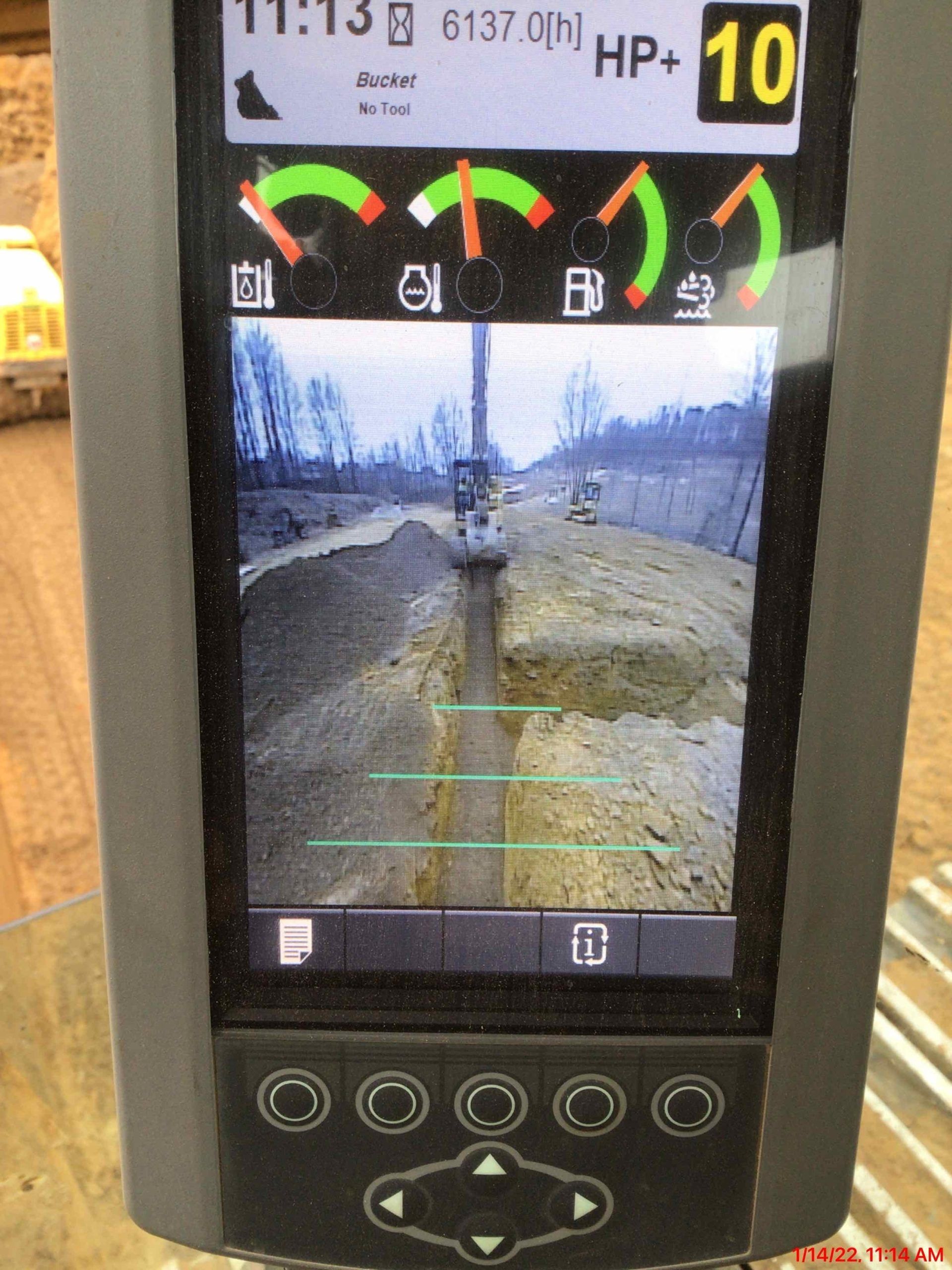 Excavator monitor showing a trench, gauges, and controls. Green and white gauges indicate levels.