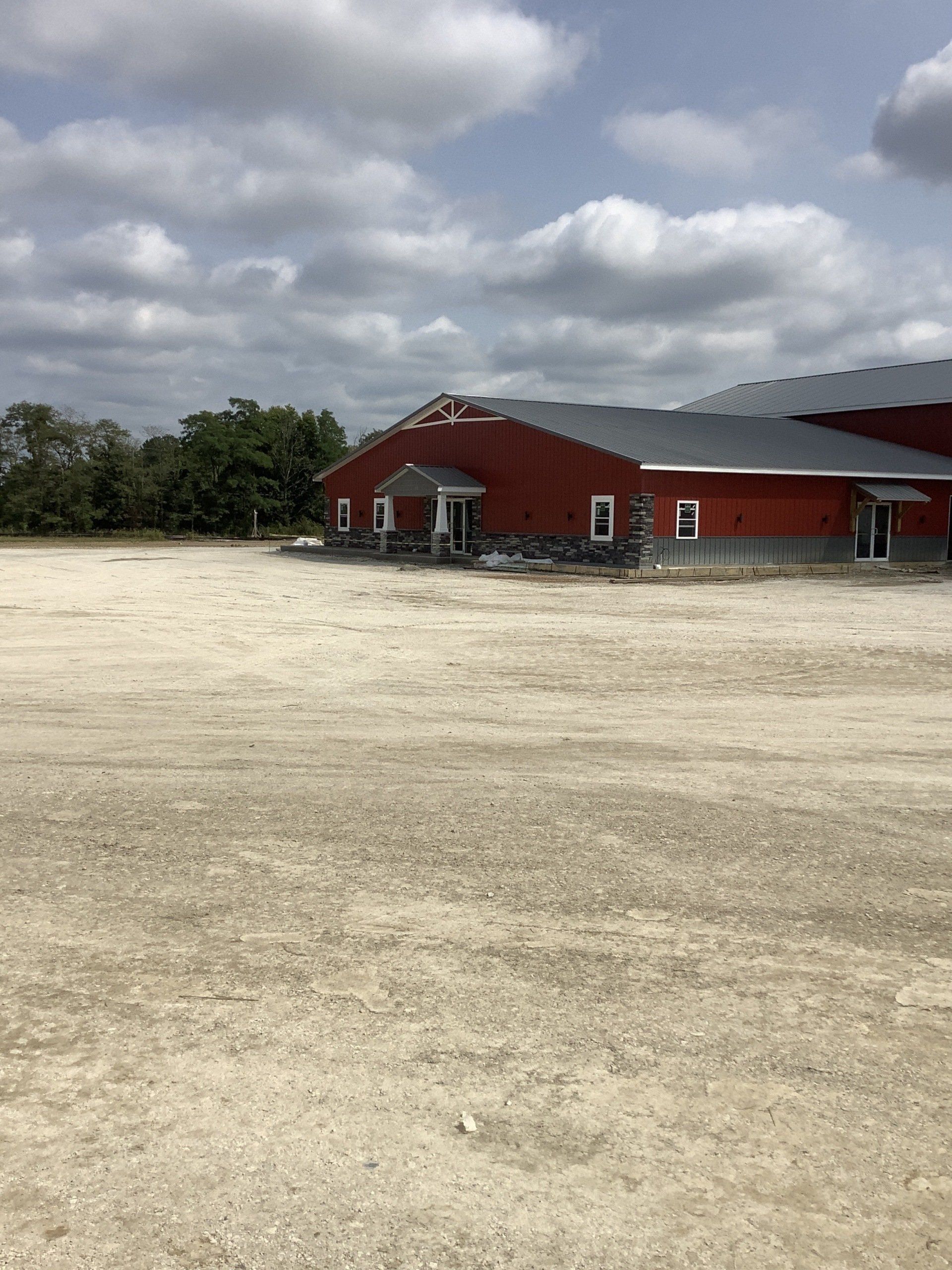 Red barn-like building with a dark roof on a gravel lot under a cloudy sky.