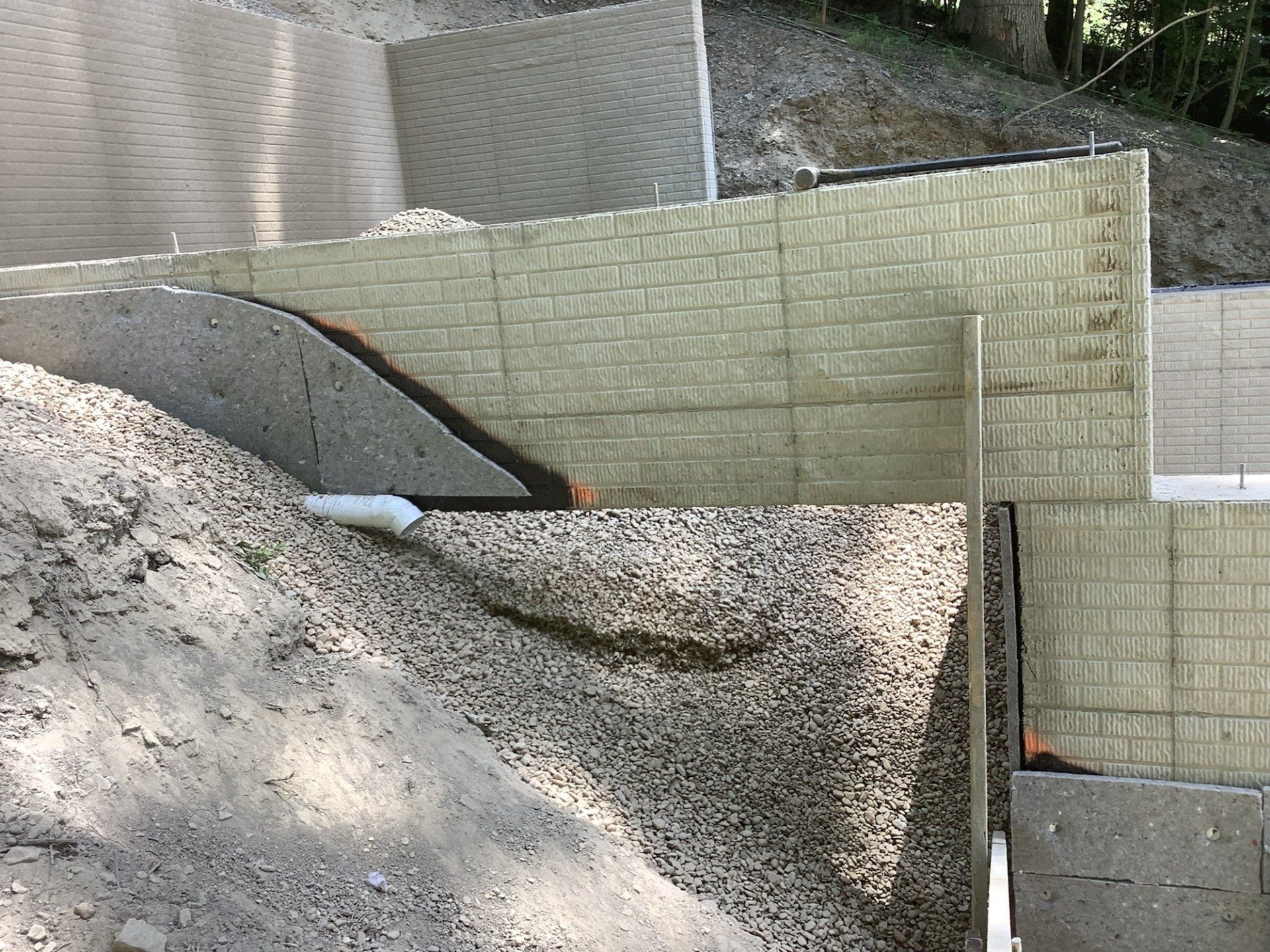 Retaining walls constructed with concrete blocks on a hillside. Gravel and drainage pipe visible.