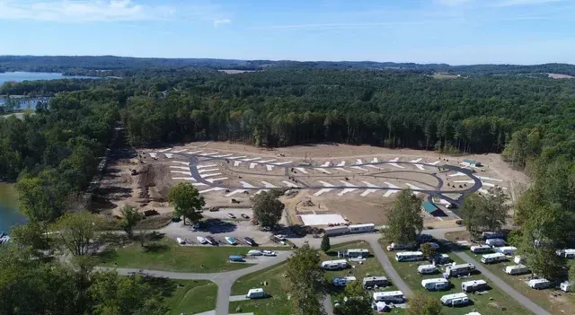 Aerial view of an RV park under construction next to a forested area and lake.