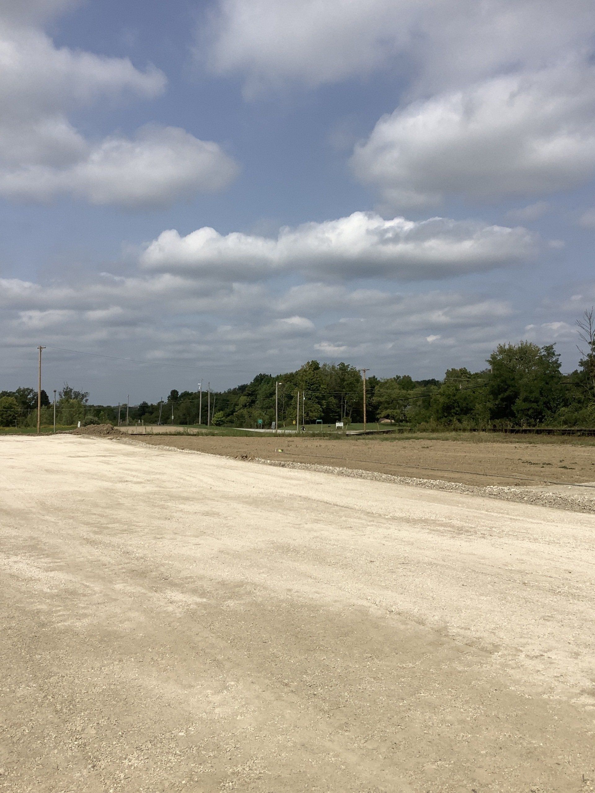 Sandy dirt road leads to trees under a cloudy sky.