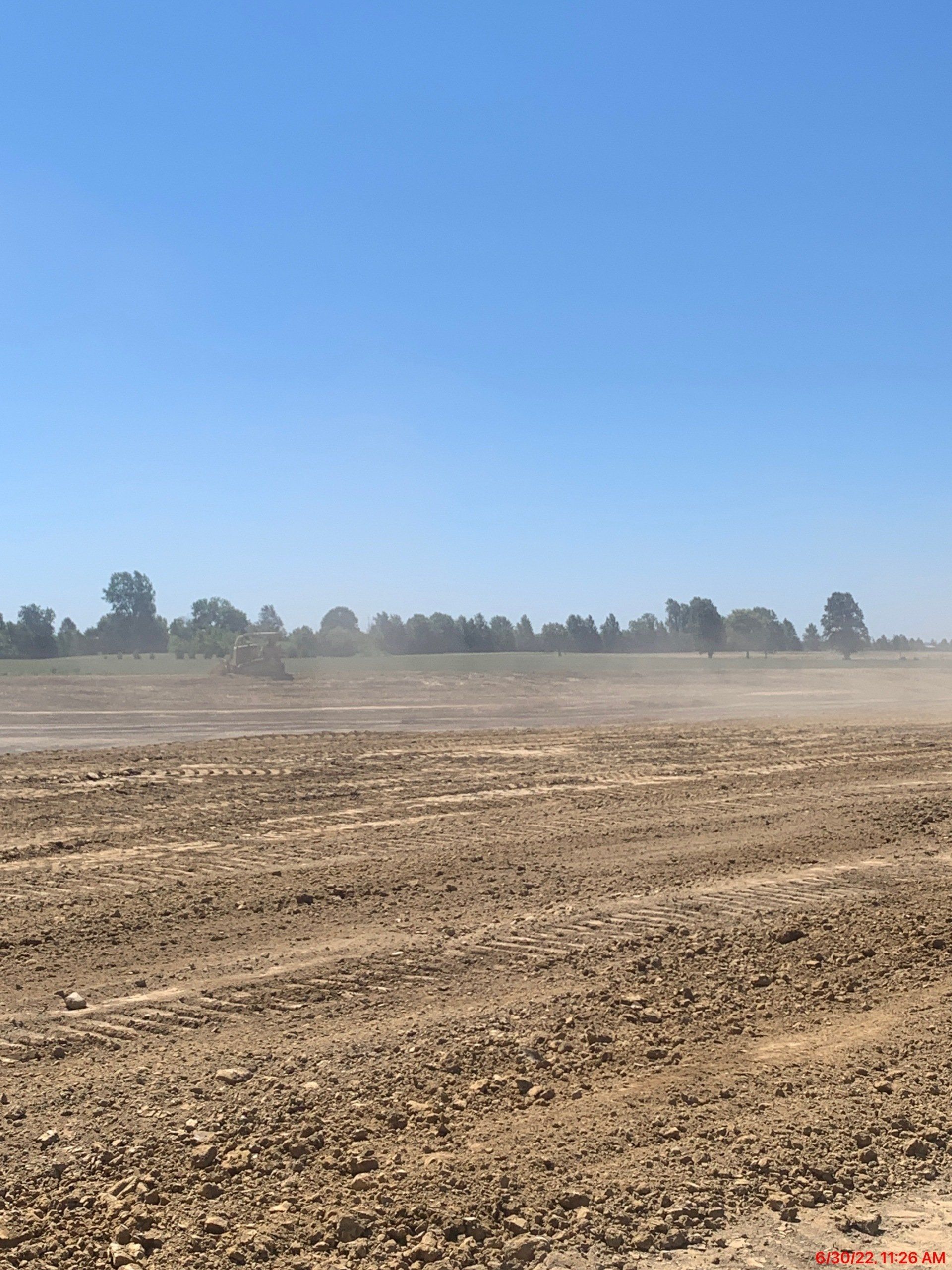 Dirt field under blue sky, trees in the distance; dust cloud rising.