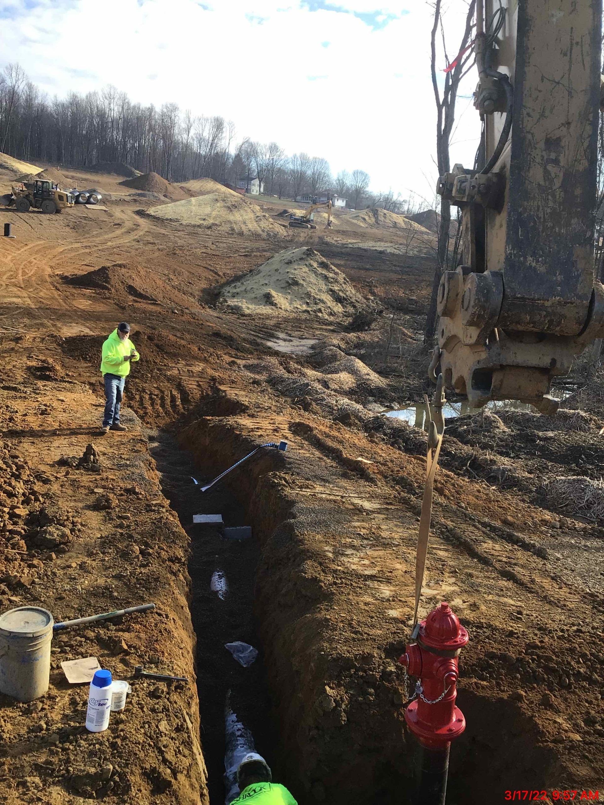Construction site: Worker by trench, fire hydrant, machinery, and hillside.