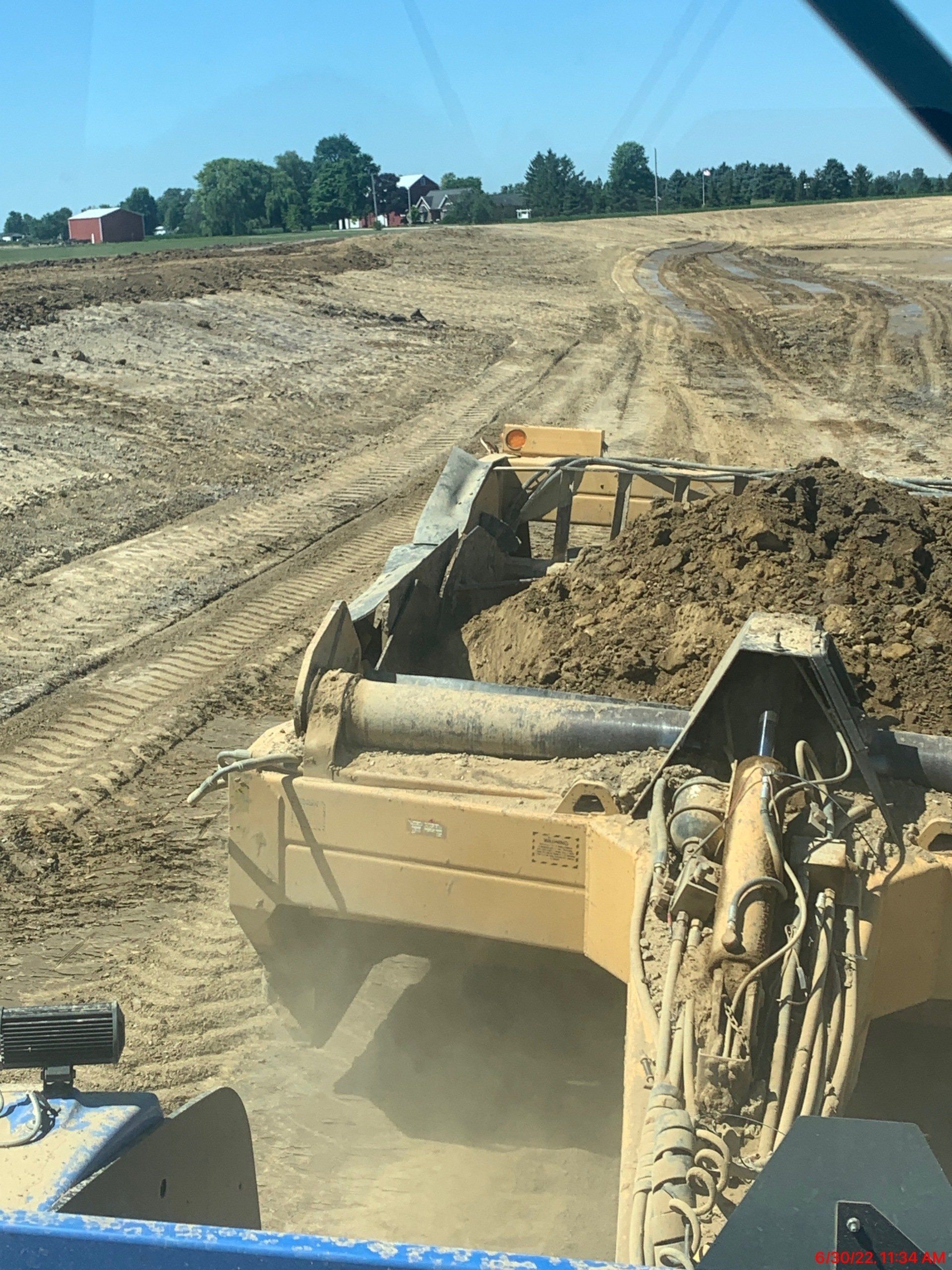 A bulldozer leveling dirt in a construction zone, with a rural landscape in the background.