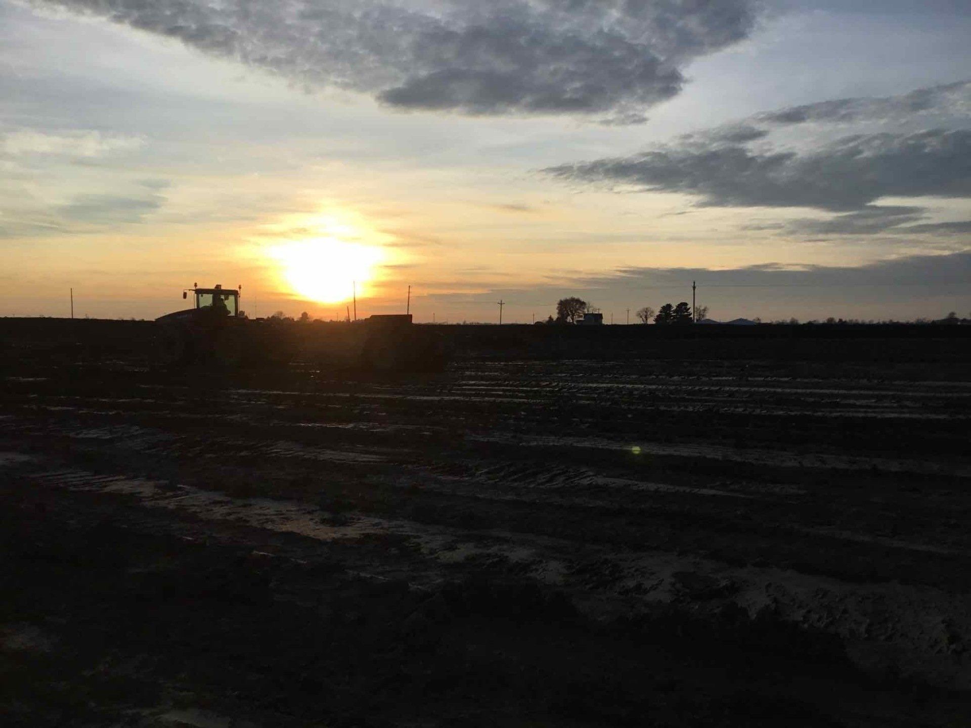 Sunrise over muddy field with tractor in silhouette.