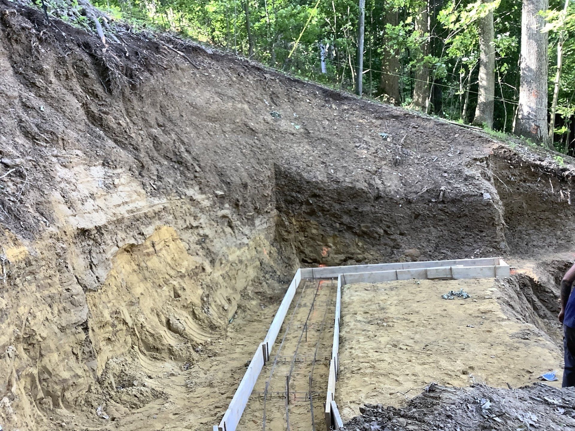 Excavated earth with concrete forms, next to a wooded hillside.