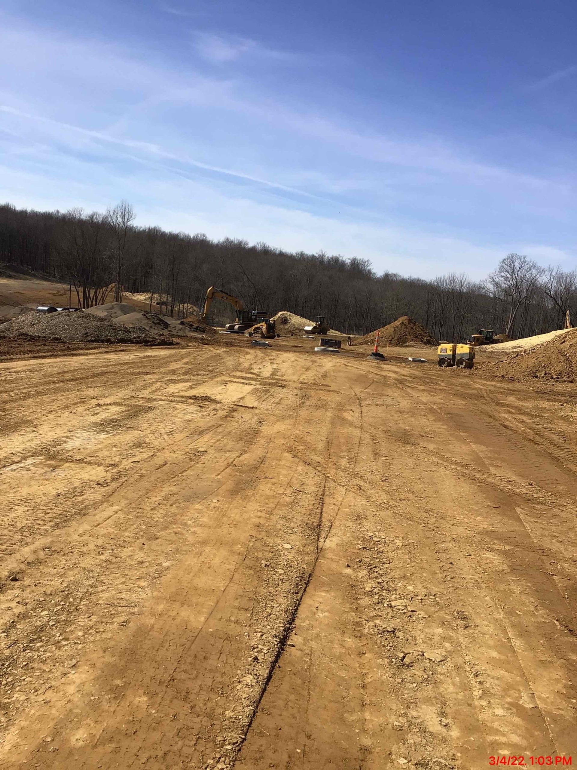 Dirt road through a construction site, heavy machinery, trees and a blue sky in the background.
