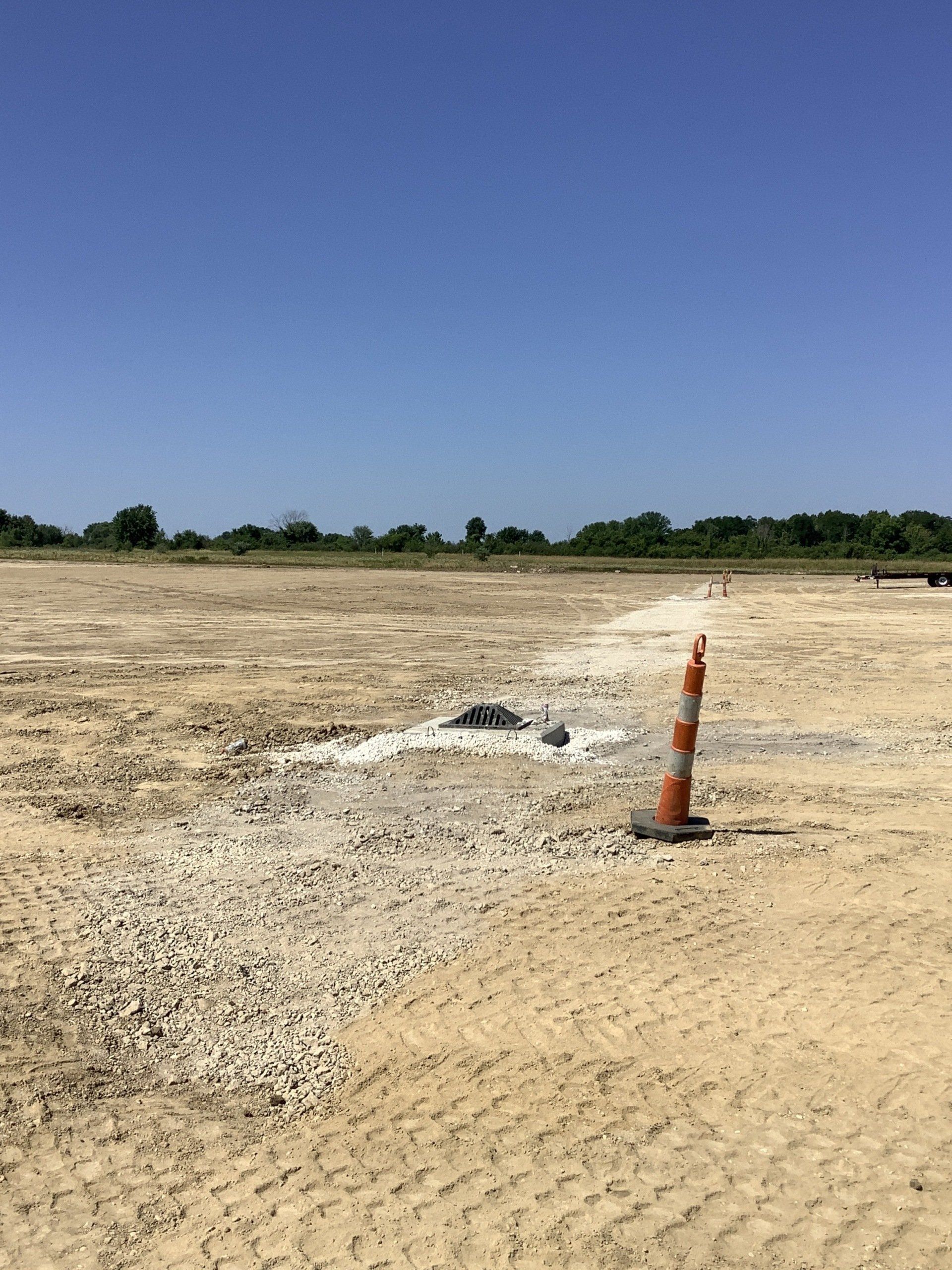 Construction site with dirt ground, a traffic cone, and a blue sky.