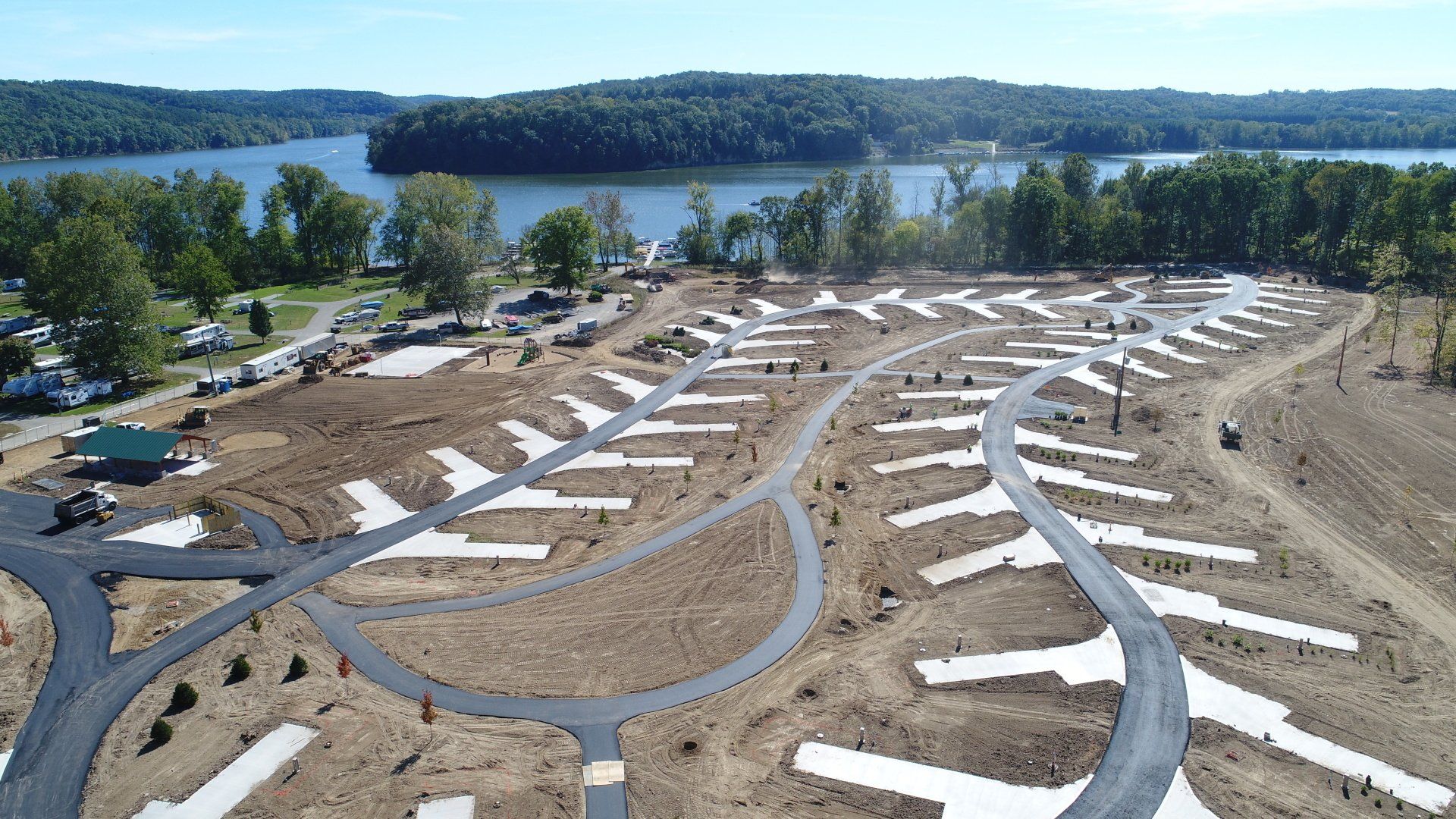 Aerial view of a partially constructed RV park near a lake. Dirt and concrete pads are visible.