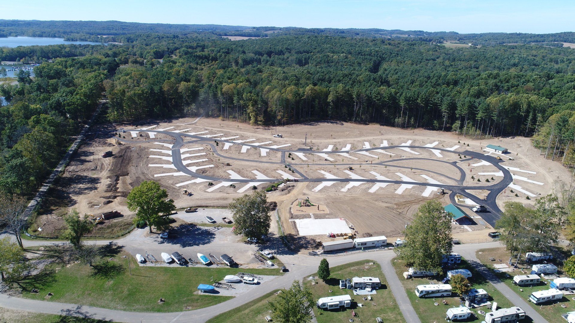 Aerial view of a campground with RV sites and paved roads surrounded by trees and a lake.