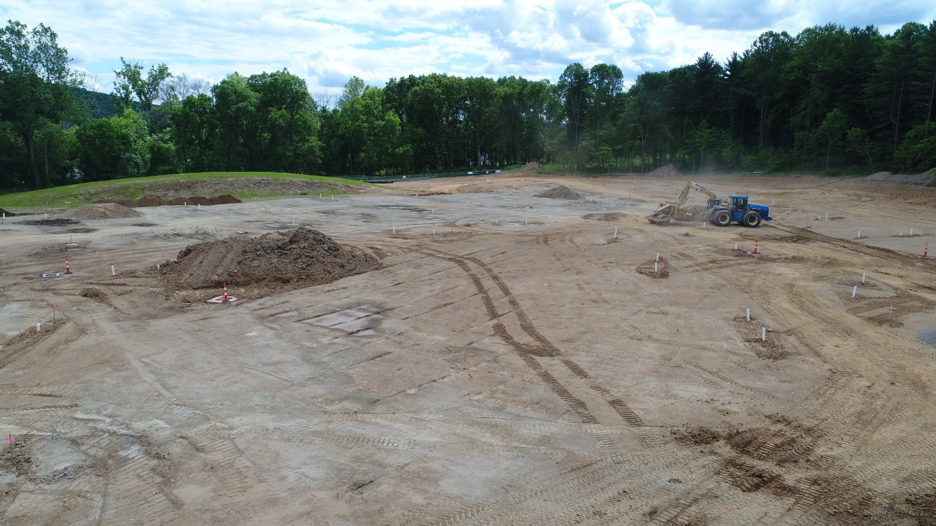 Construction site with dirt piles and tractor, surrounded by trees.
