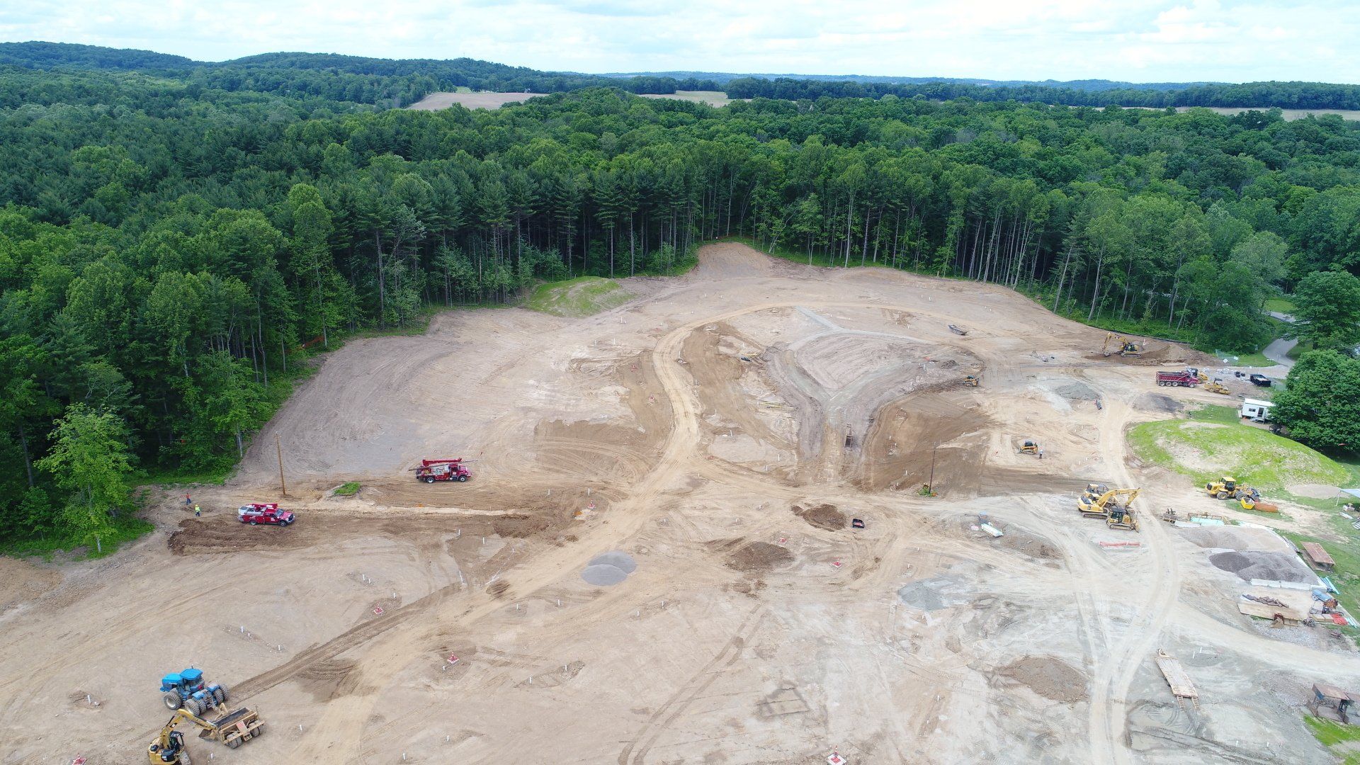 Construction site clearing trees with heavy machinery, adjacent to a forest.