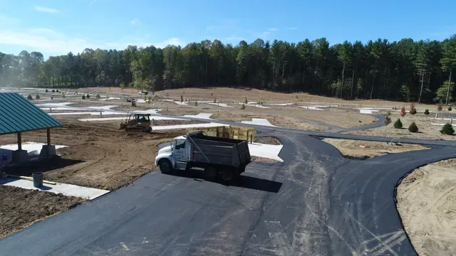 A dump truck on newly paved road at a construction site with trees and a small building.