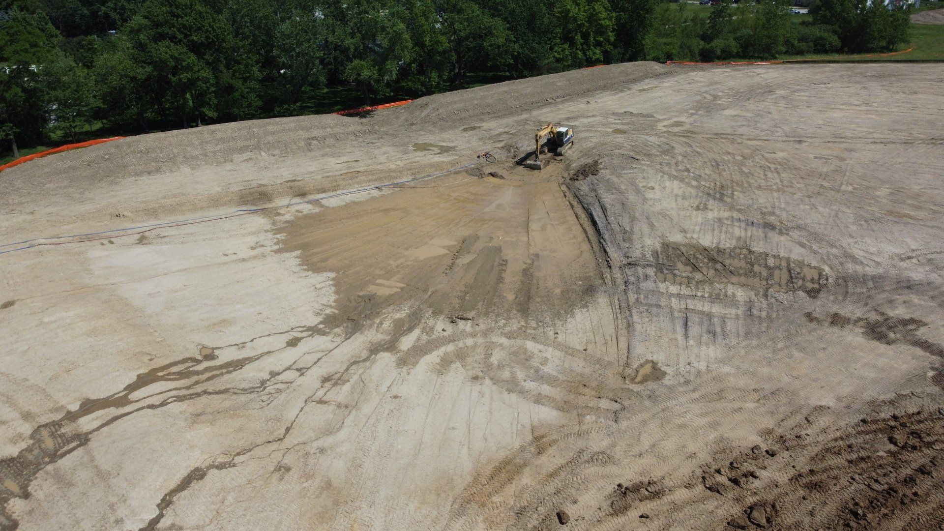 Dirt field with mud and water runoff, trees in background, small construction vehicle.