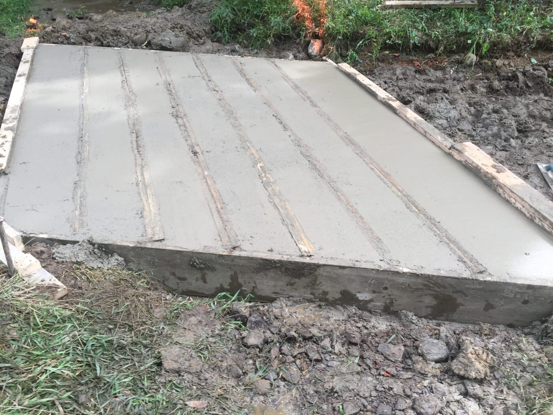 Freshly poured concrete slab with wooden formwork, outdoors.