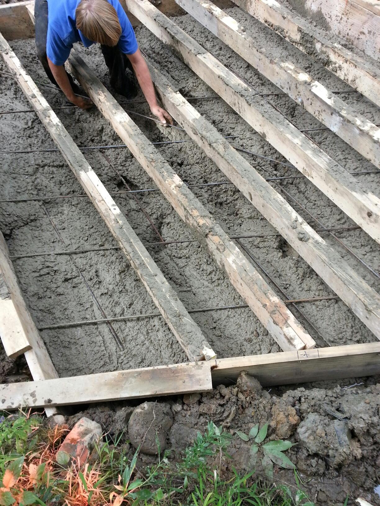 Person laying cement between wooden beams in a construction project.