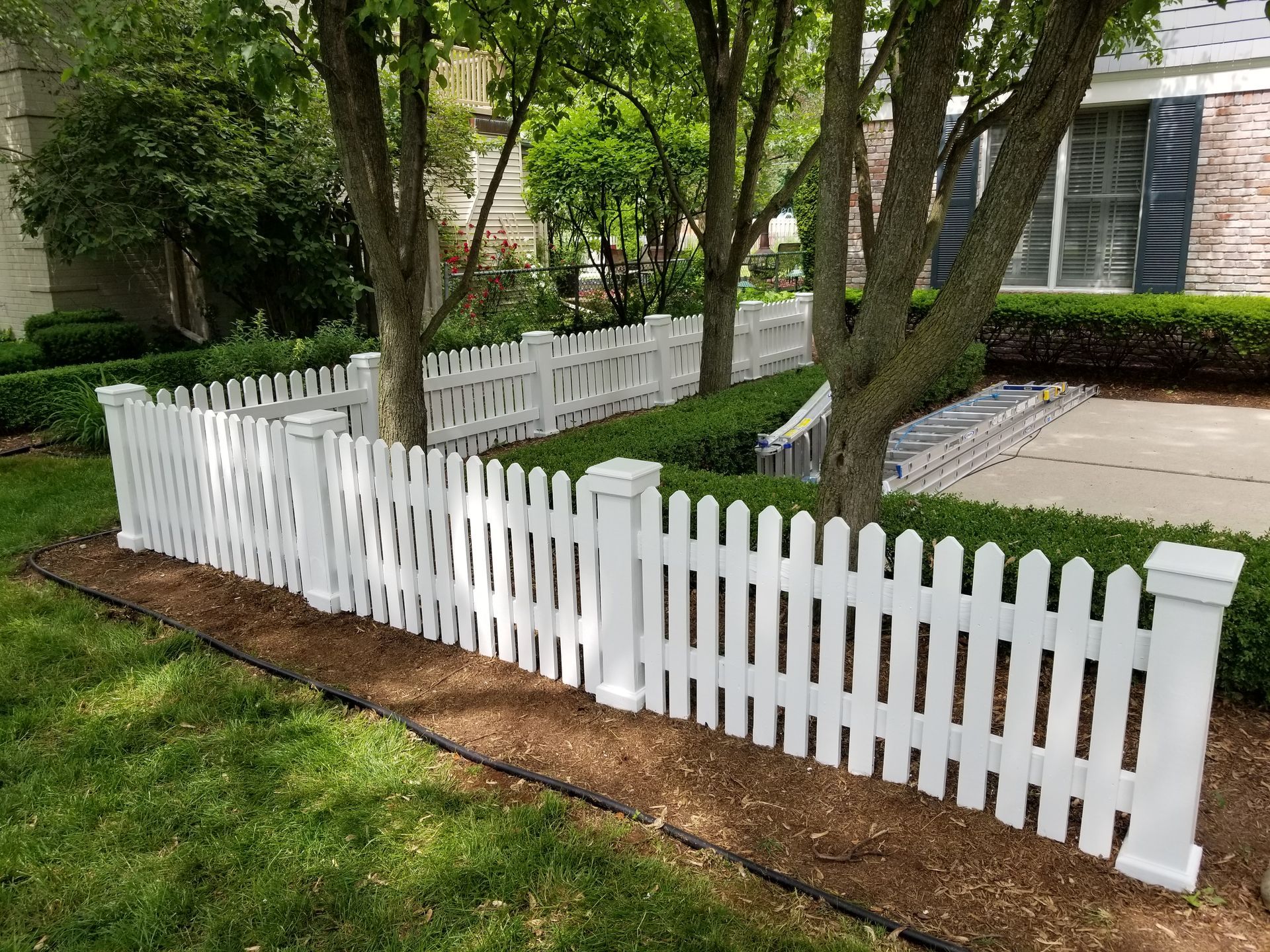 A white picket fence surrounds a lush green yard in front of a house.