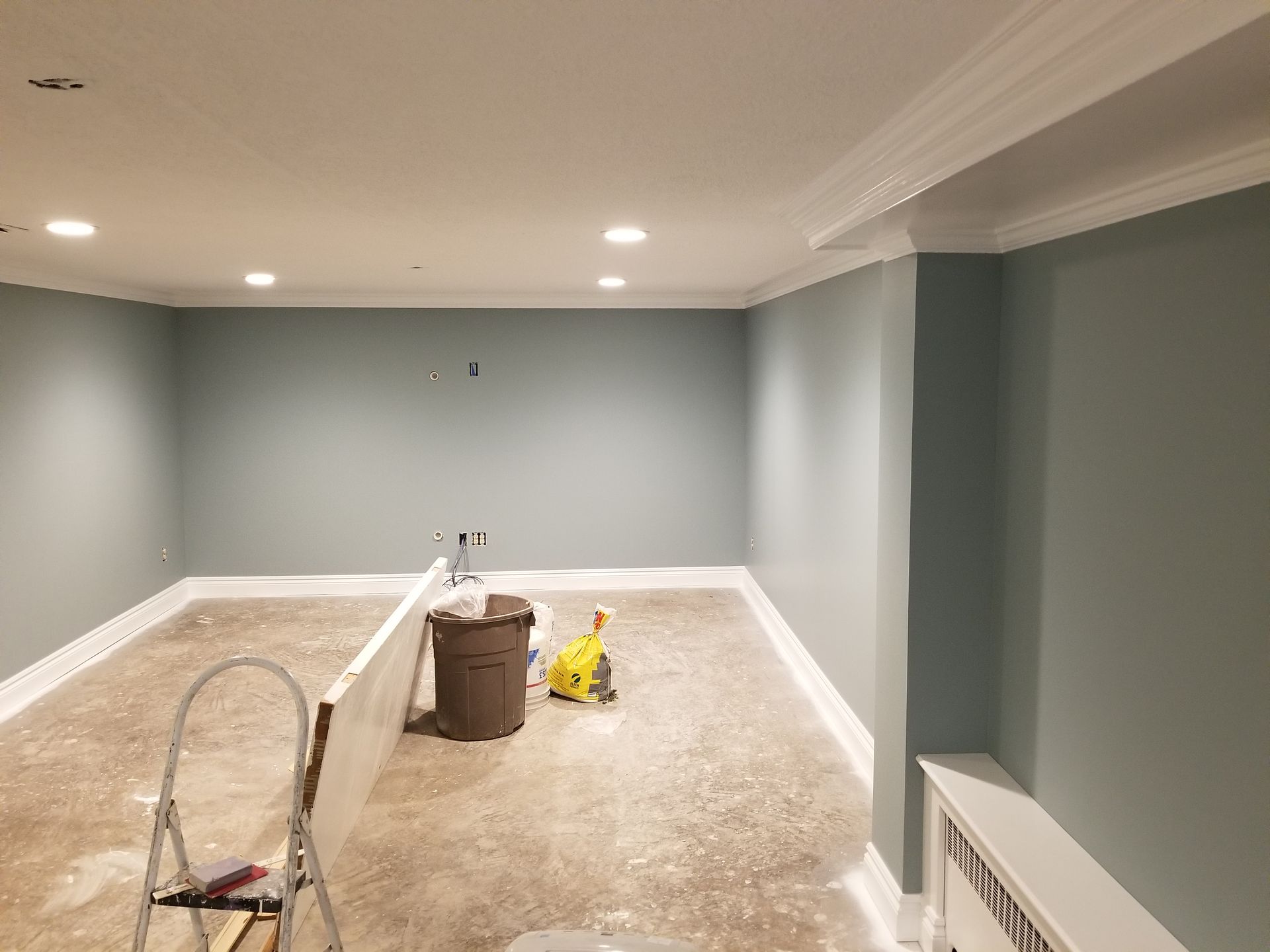 A room with a ladder and a trash can in it.