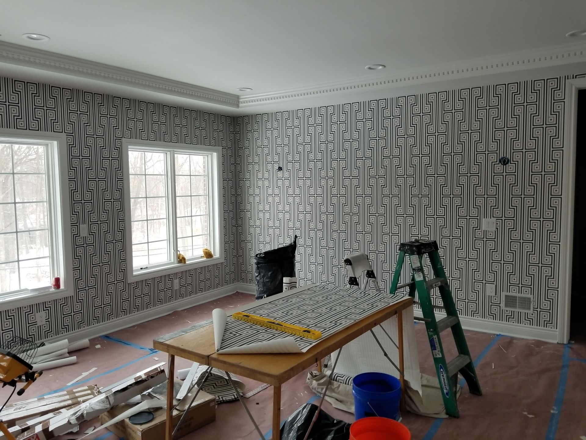 A room with a table and a ladder in front of a wall covered in wallpaper.
