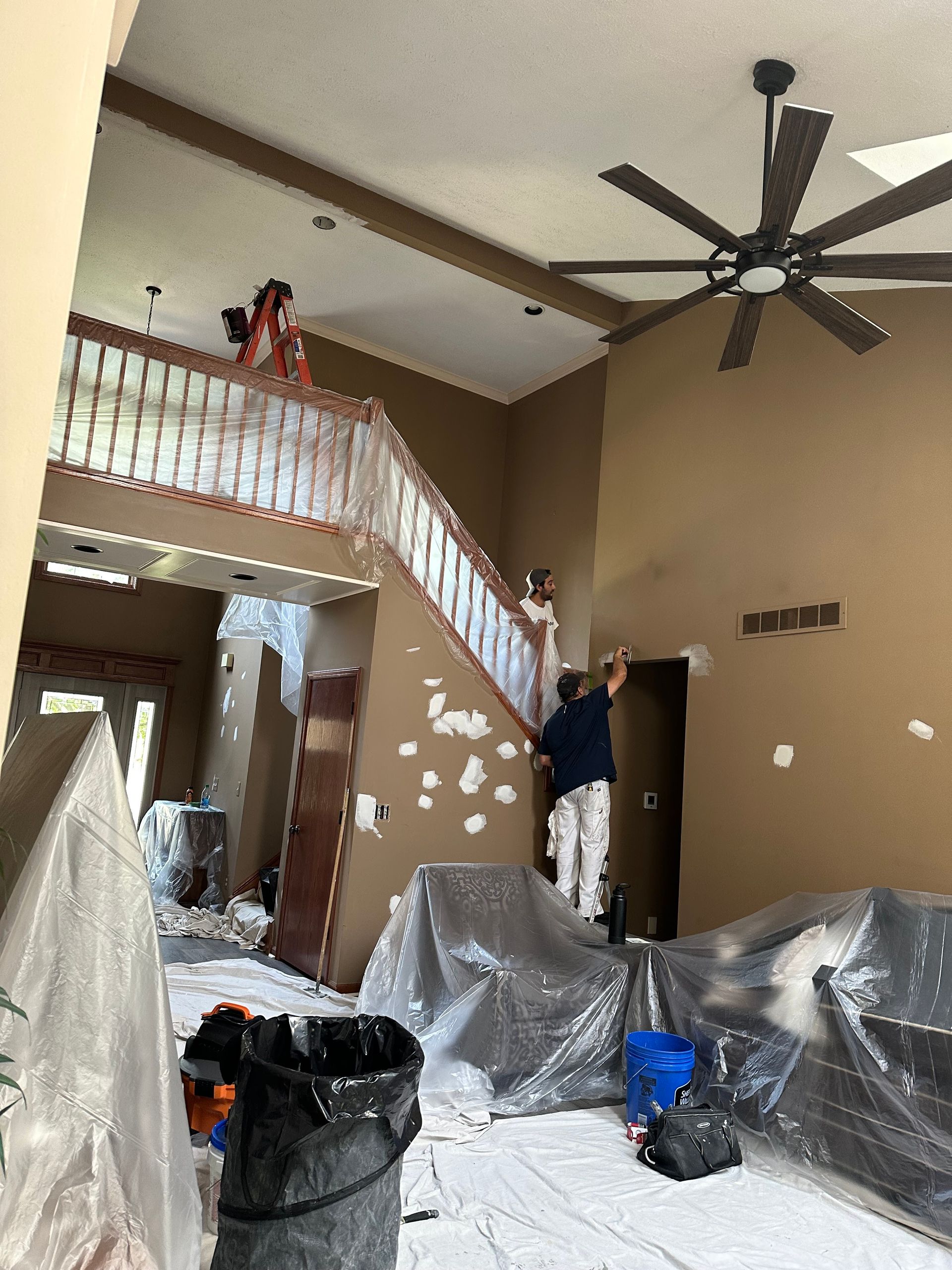A man is painting a wall in a living room with a ceiling fan.