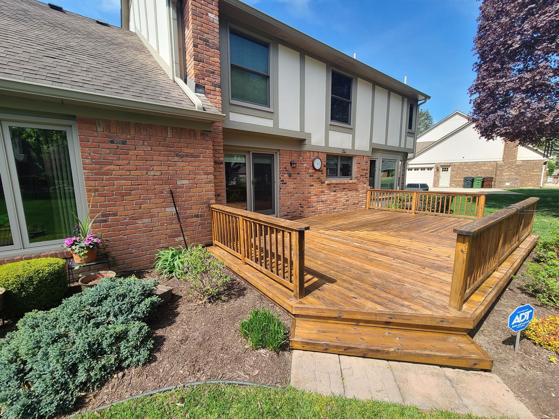 A large wooden deck is in front of a brick house.